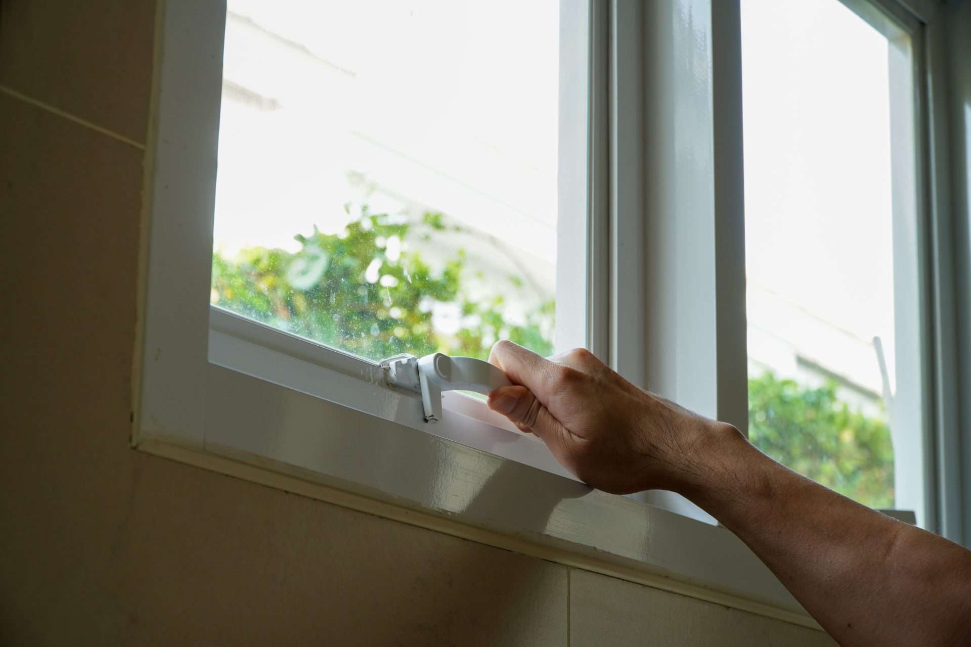 Close-up of a hand reaching up to adjust the crank at the bottom of a casement window