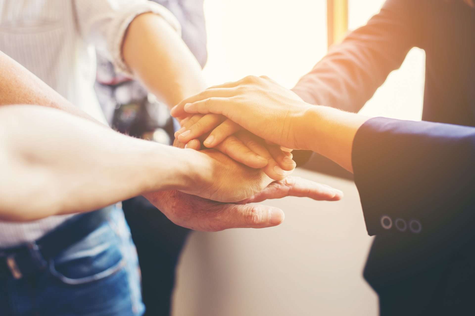 Five people placed one hand each in the middle, stacked on top of one another to signify teamwork.