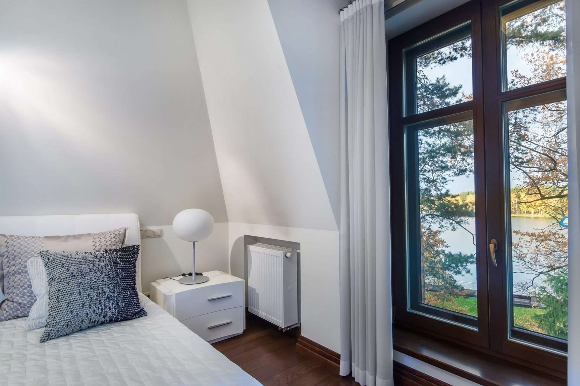 Bright bedroom with a bed, pillows, nightstand, and rich wood casement windows
