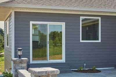 A modern home exterior featuring gray siding with a white-trimmed sliding glass patio door and a square window.
