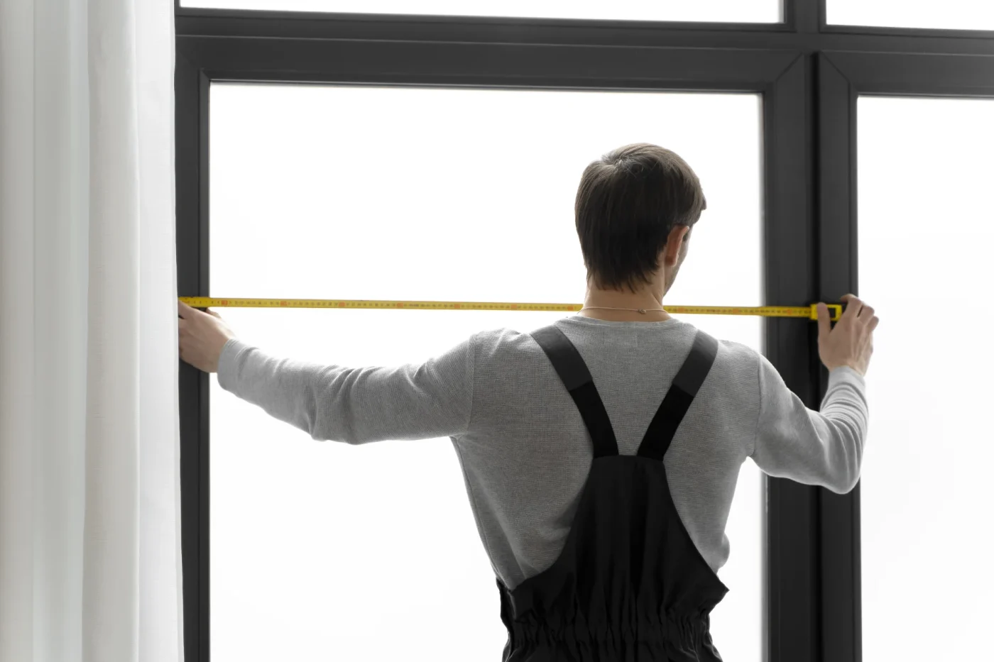 Professional installer measuring a high-end window with a charcoal frame and frosted glass.