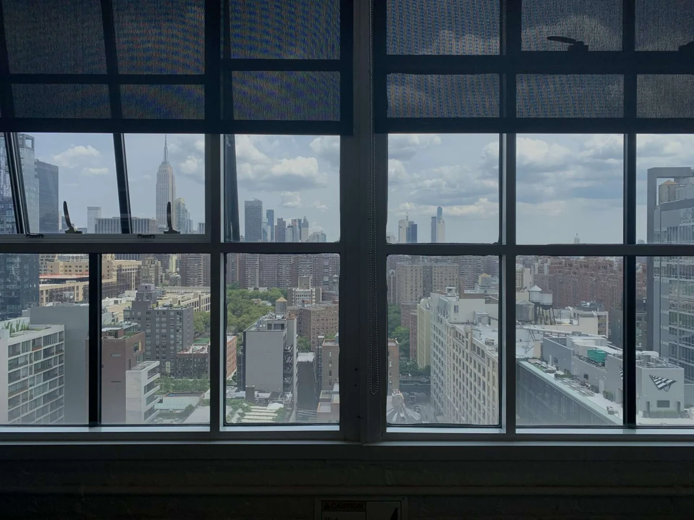 Premium Aluminum Windows | Greenwich, CT | Rockman Windows and Doors Black-framed aluminum windows with dark shades overlooking the New York City skyline, the Empire State Building, rooftops, water towers, and clouds.